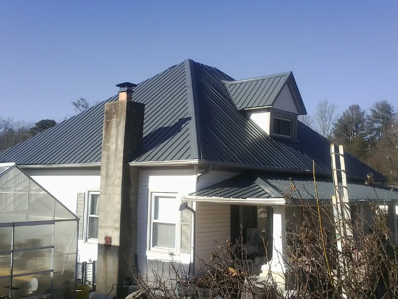 Dark blue standing seam metal roof on a white farmhouse with dormer — Slate & Tile Roof Repair by Roofing Brothers in Rubicon