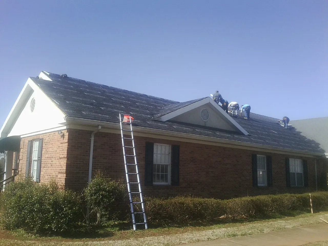 Crew tearing shingles off a brick ranch roof with a ladder set — Metal Roof Repair work by our crew in Rubicon