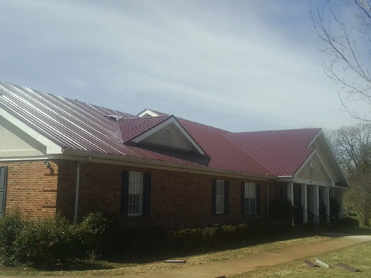 Red metal roof with gabled entries on a long brick building, from a Hail Damage Roof Repair job in Rubicon