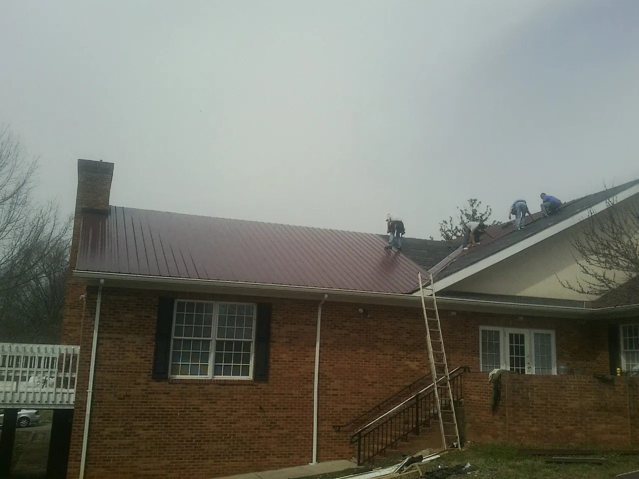 Crew setting red metal roofing panels on a brick home in Rubicon