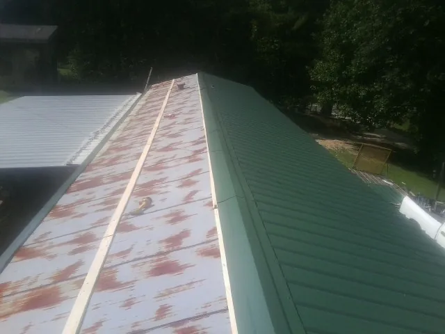 Old rusted panels beside newly installed green metal roofing — Wind Damage Roof Repair by Roofing Brothers in Rubicon