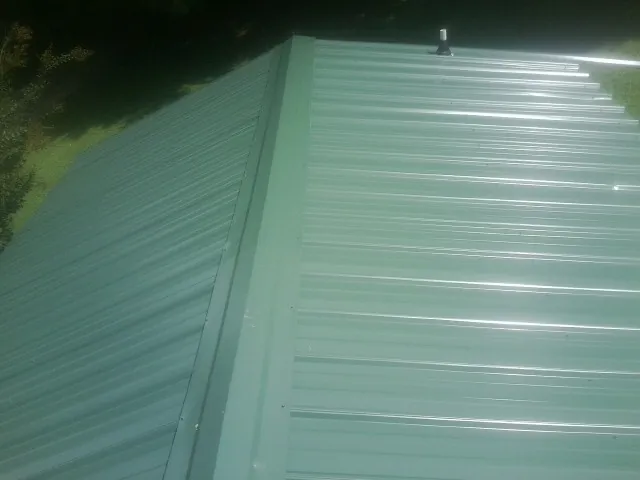 New green metal panels meeting at the ridge of a roof — Flat Roof Repair work by our crew in Rubicon