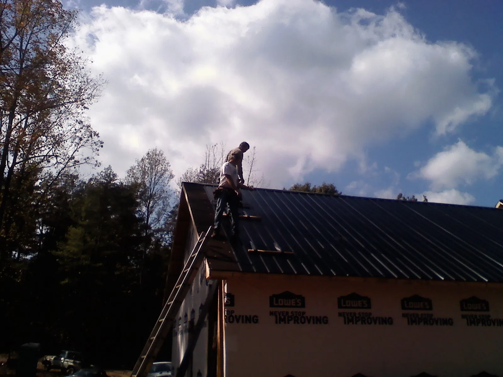 Roofer fastening dark metal panels high against a cloudy sky, from a Roof Inspection job in Rubicon